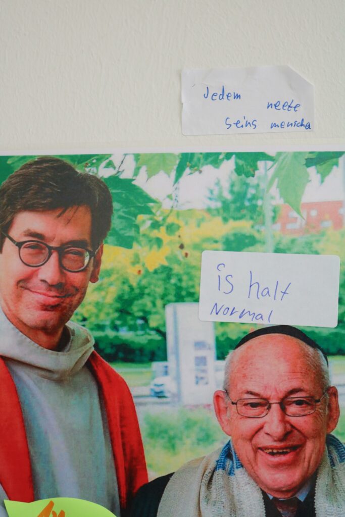 Zwei Personen lächeln vor grünem Hintergrund, mit handgeschriebenen Notizen.