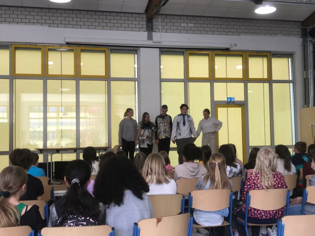Schüler stehen auf der Bühne, Zuschauer sitzen im Publikum.