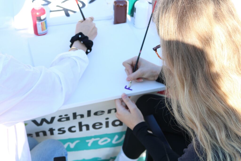 Schülerinnen bemalen einen Tisch mit Pinsel und Farbe.