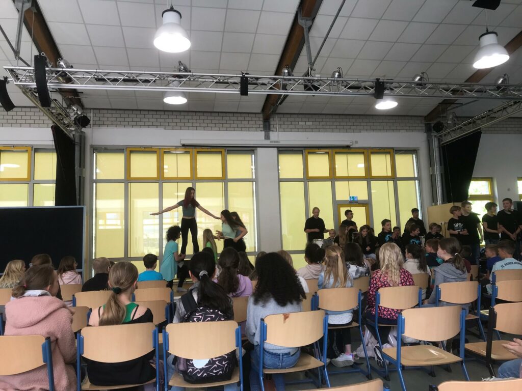 Schüler führen eine Aufführung vor einer sitzenden Zuschauergruppe auf.