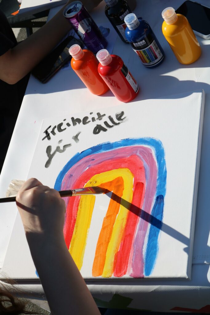 Hand, die mit Pinsel ein buntes Regenbogenbild auf Leinwand malt.