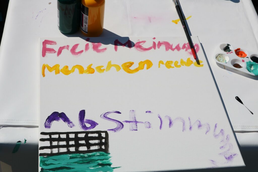 Bunt bemalte Leinwand mit Text und Farbklecksen.