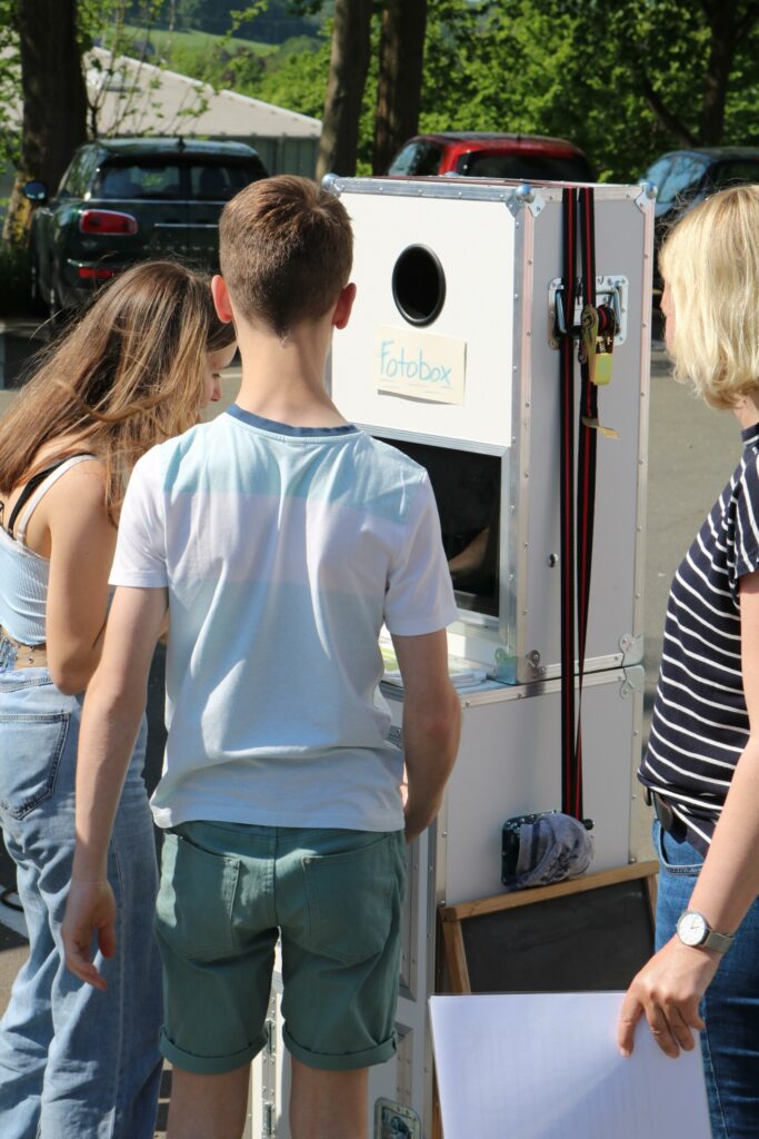 Menschen stehen vor einem Stand mit einem kleinen Fenster und einem Schild.
