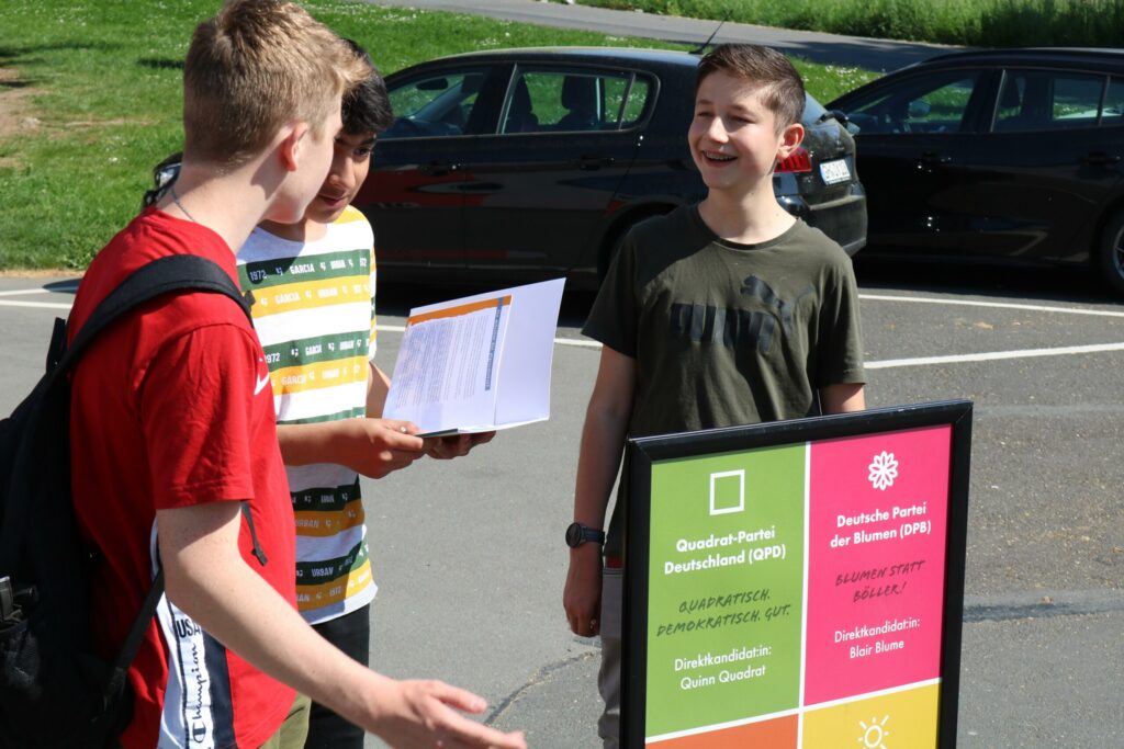 Drei Schüler stehen vor einem Informationsschild auf dem Schulgelände.