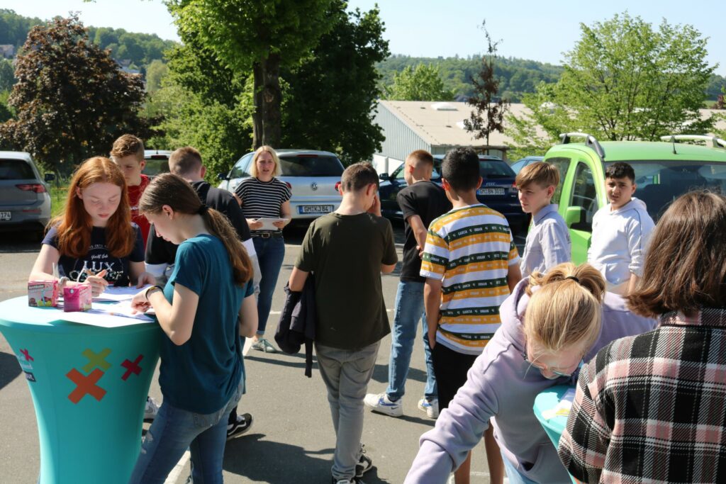 Schüler stehen an einem Tisch im Freien und tauschen sich aus.