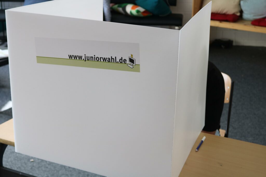 Wahlurne mit dem Logo der Juniorwahl auf einem Tisch.