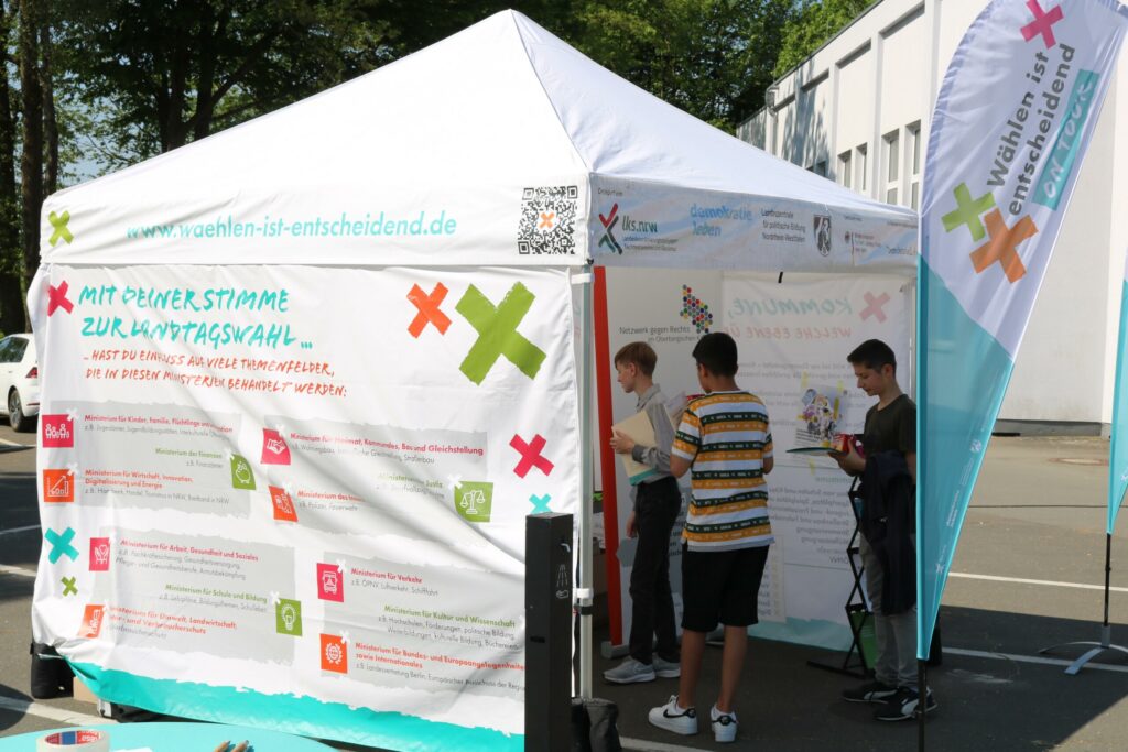 Informationsstand mit plakatierter Wand und mehreren Personen.