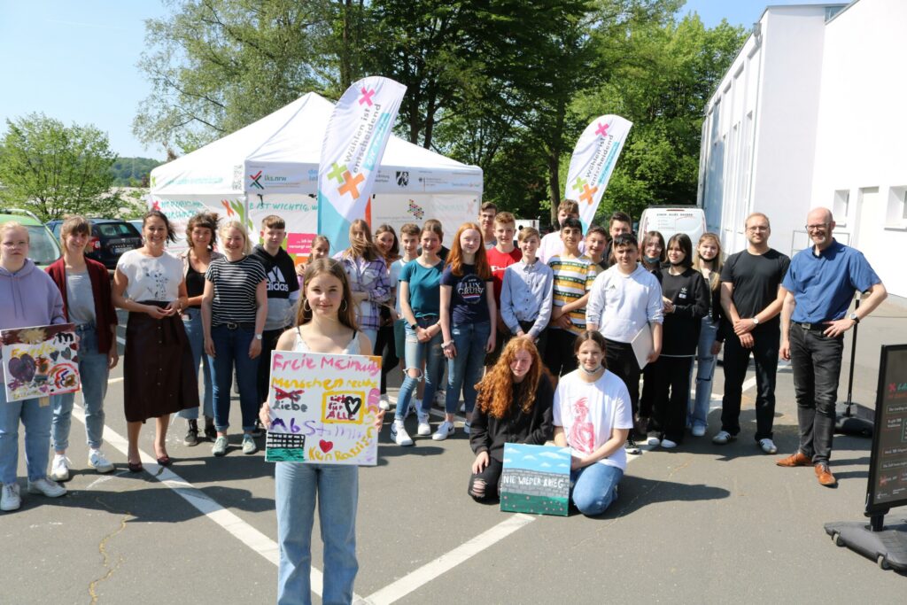 Gruppe von Schülern und Lehrern vor einem Zelt mit Bannern, lächelnd und posierend.