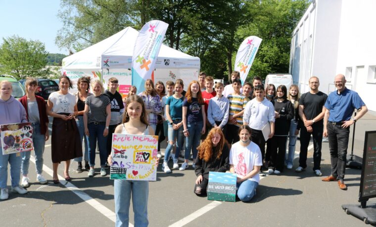 Gruppe von Schülern und Lehrern vor einem Zelt mit Bannern, lächelnd und posierend.
