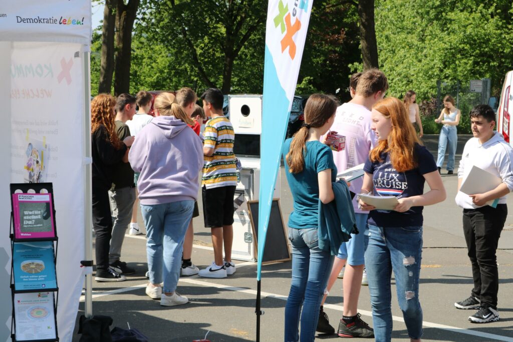 Schülerinnen und Schüler stehen an Informationsständen im Freien und sprechen miteinander.