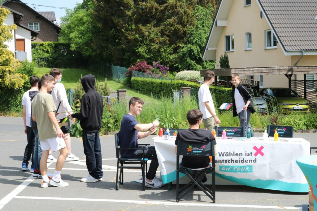 Schüler stehen an einem Tisch im Freien und nehmen an einer Umfrage teil.