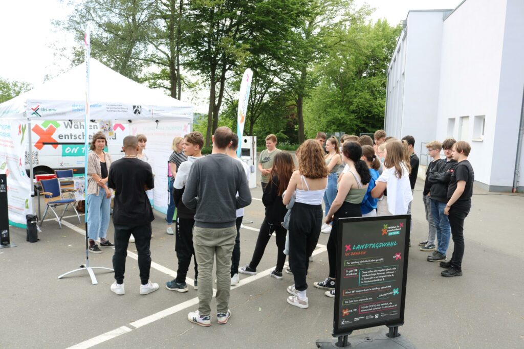 Schüler stehen vor einem Informationsstand unter einem Zeltdach.