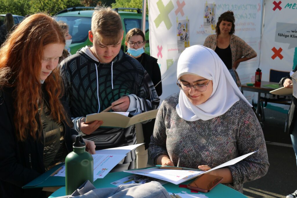 Schülerinnen und Schüler lesen in Büchern an einem Stehtisch im Freien.