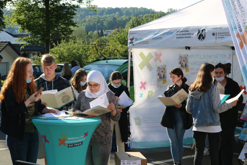 Schülerinnen und Schüler stehen an einem Info-Stand und halten Bücher in der Hand.