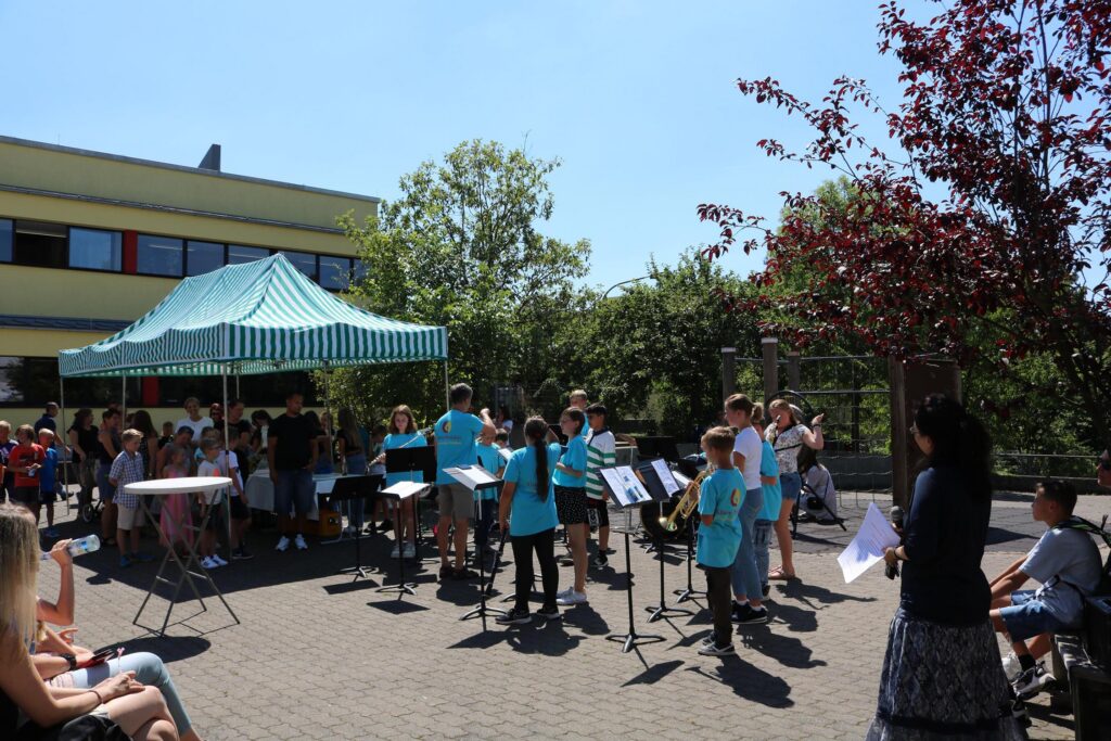 Schüler spielen Musik unter einem Zeltdach, Publikum sitzt im Hintergrund.