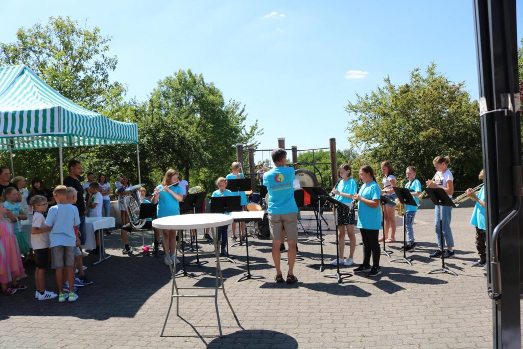 Schülerband spielt im Freien unter einem Pavillon. Kinder hören zu.