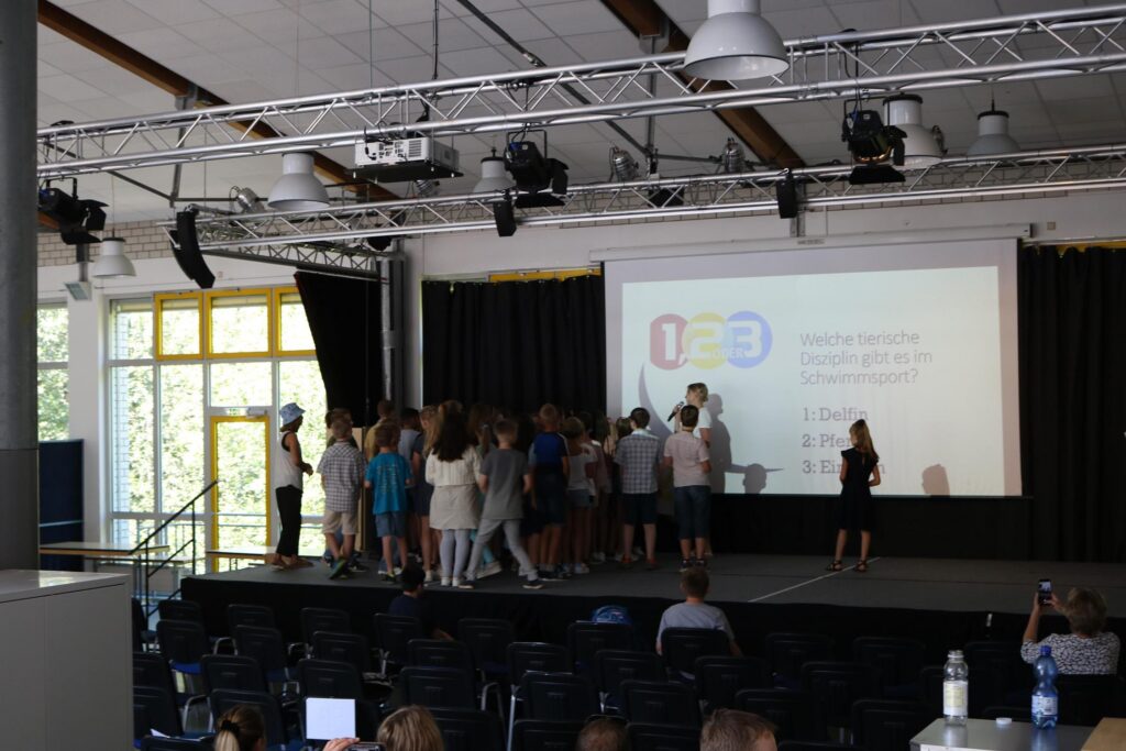 Gruppe von Schülern auf der Bühne vor einer Projektorleinwand.