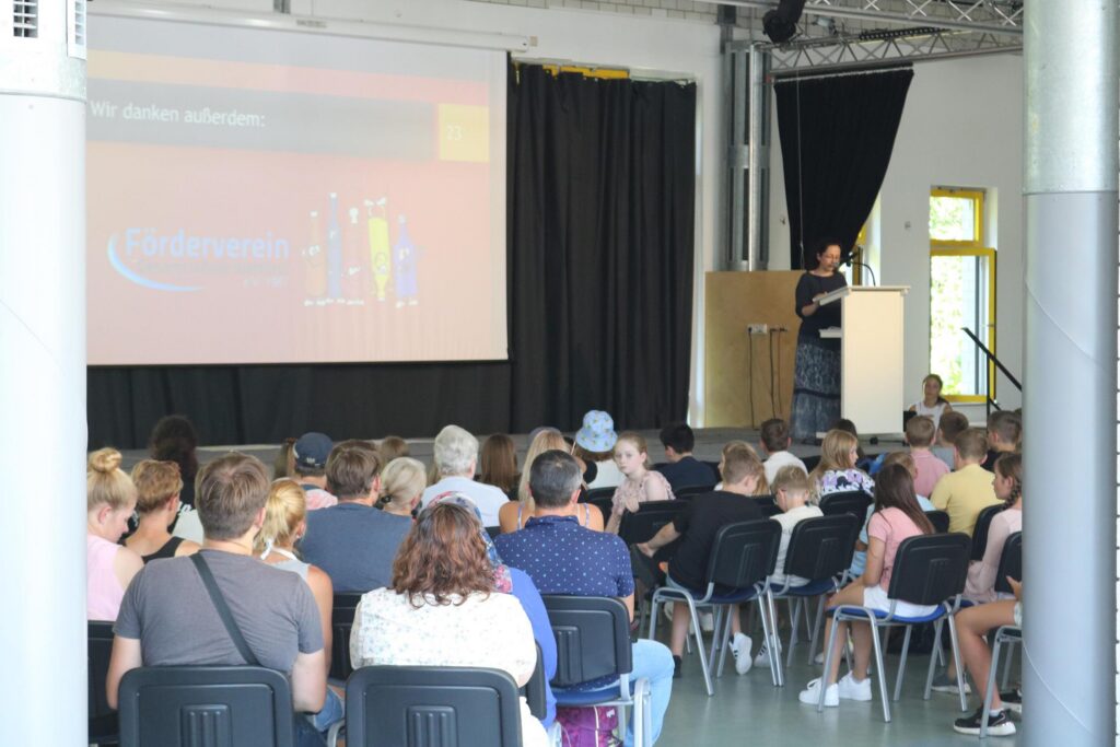 Vortrag in einem Saal mit Publikum und einer Präsentation im Hintergrund.