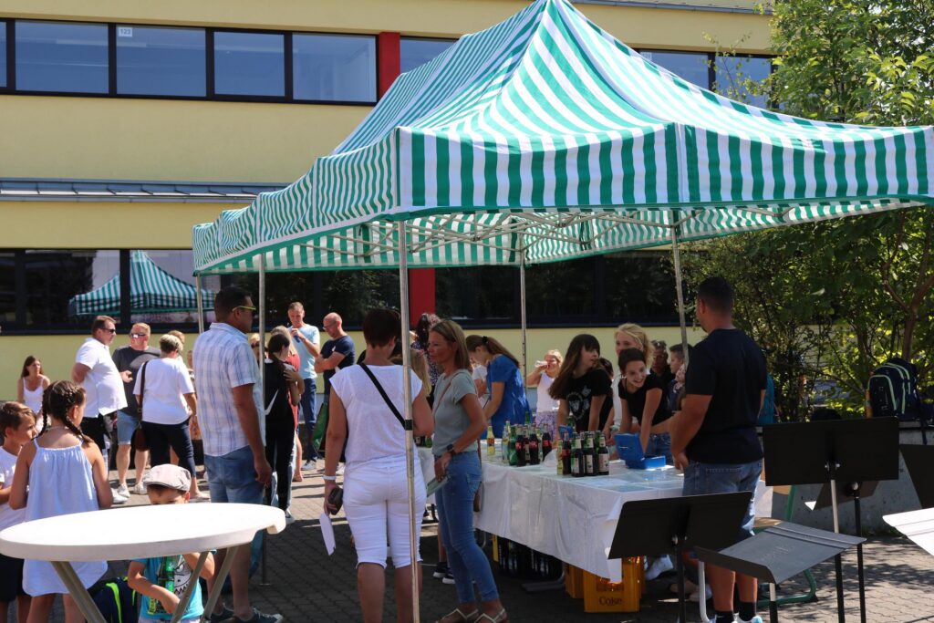 Marktstand mit Zeltdach, viele Menschen stehen um Tische mit Getränken.