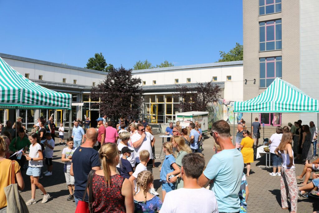 Menschenmenge bei einem Fest im Freien mit Zelten und sonnigem Wetter.