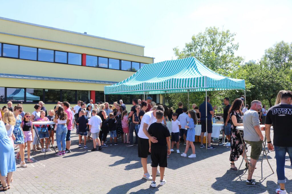 Viele Kinder und Erwachsene stehen unter einem Zelt auf dem Schulhof.
