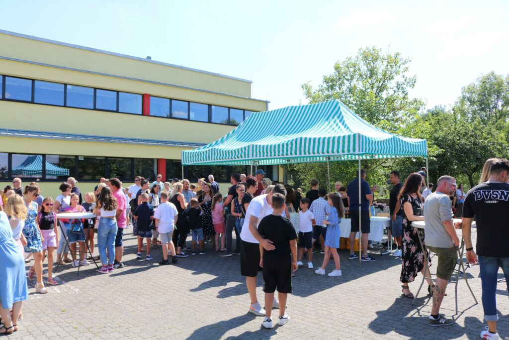 Schüler und Erwachsene versammeln sich unter einem Zelt auf dem Schulgelände.