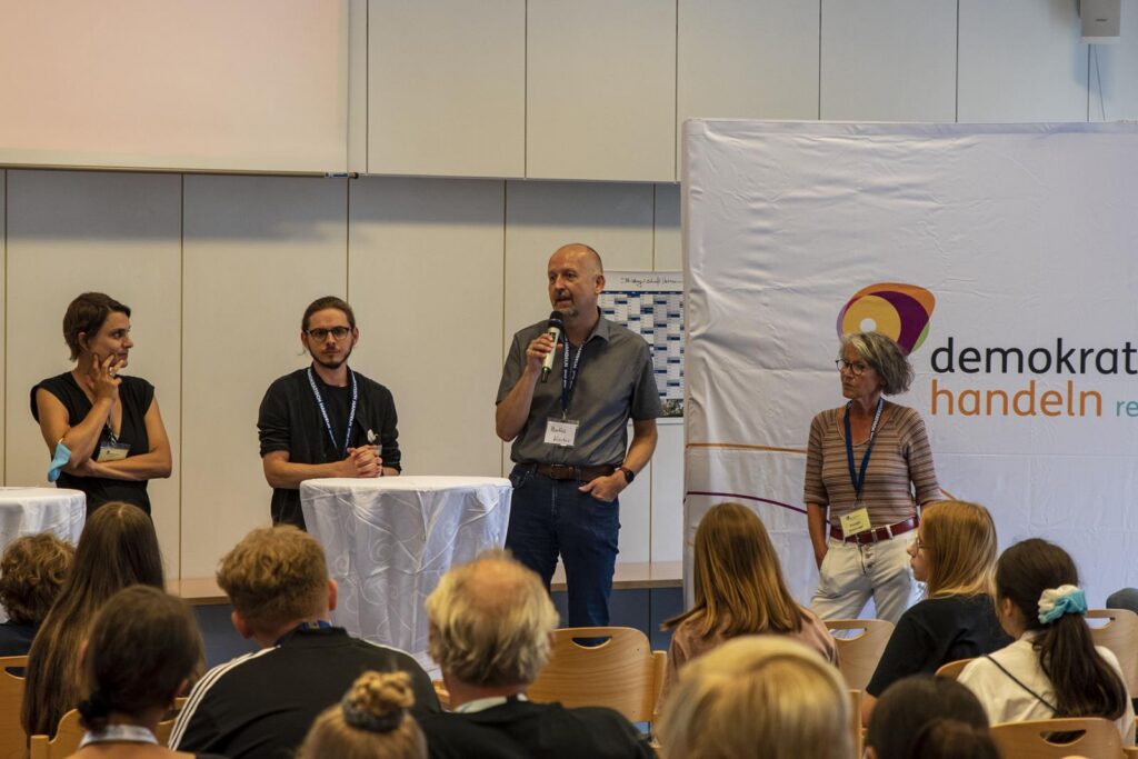 Diskussionsteilnehmer stehen an Stehtischen bei einer Veranstaltung.