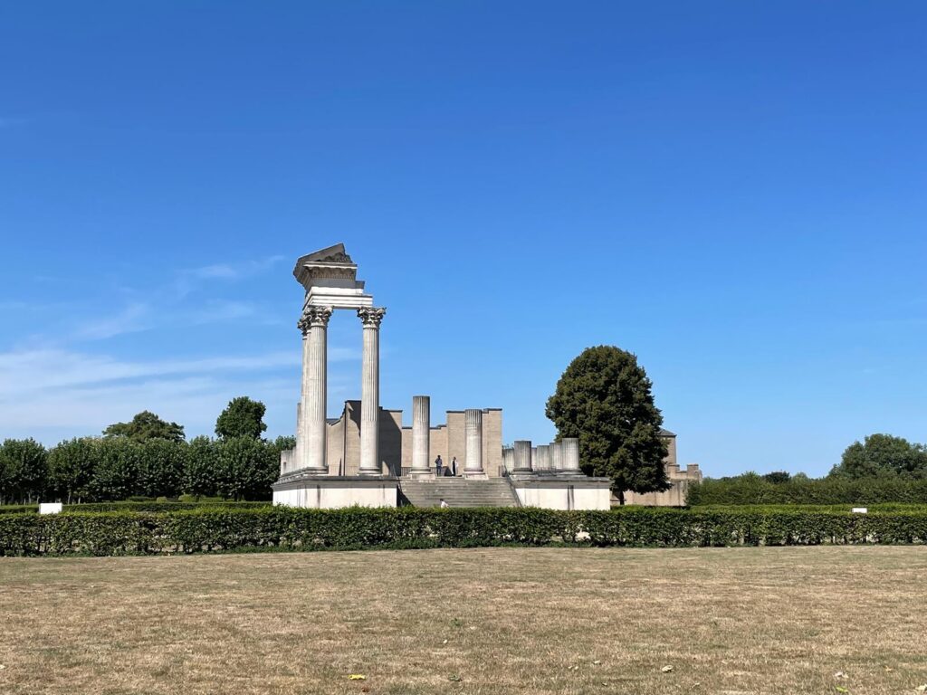 Ruinen eines antiken Gebäudes vor blauem Himmel und grünen Bäumen.