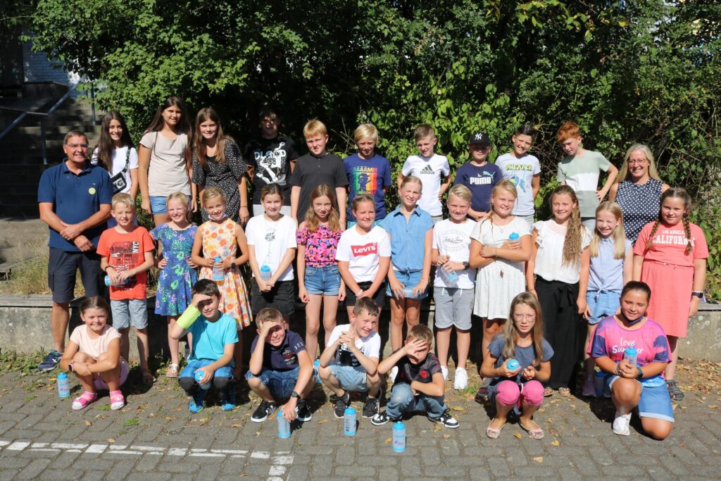 Schülergruppe steht draußen auf einem Schulhof bei sonnigem Wetter.