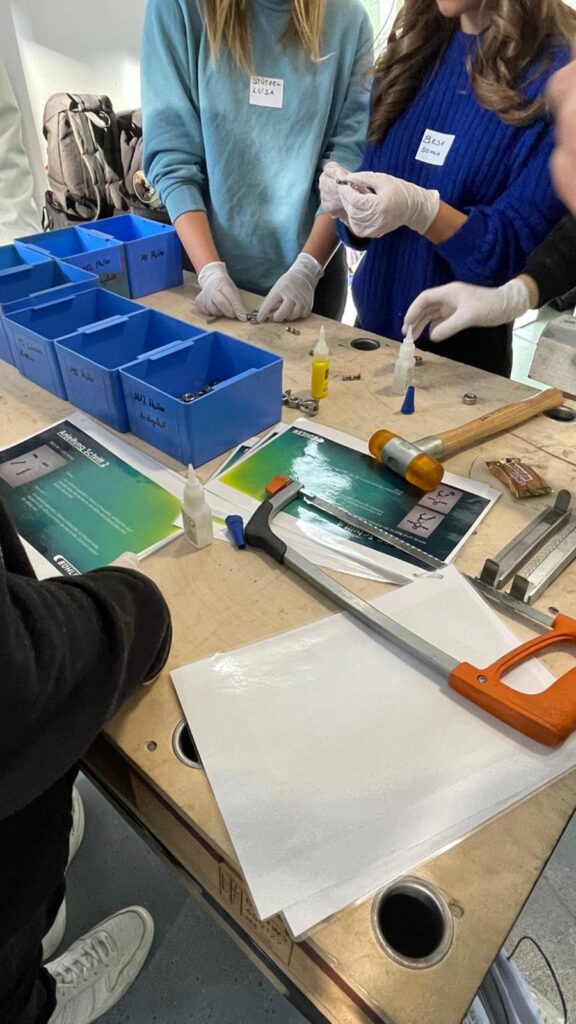 Tische mit Werkzeugen und Materialien für praktische Experimente. Schüler arbeiten zusammen.