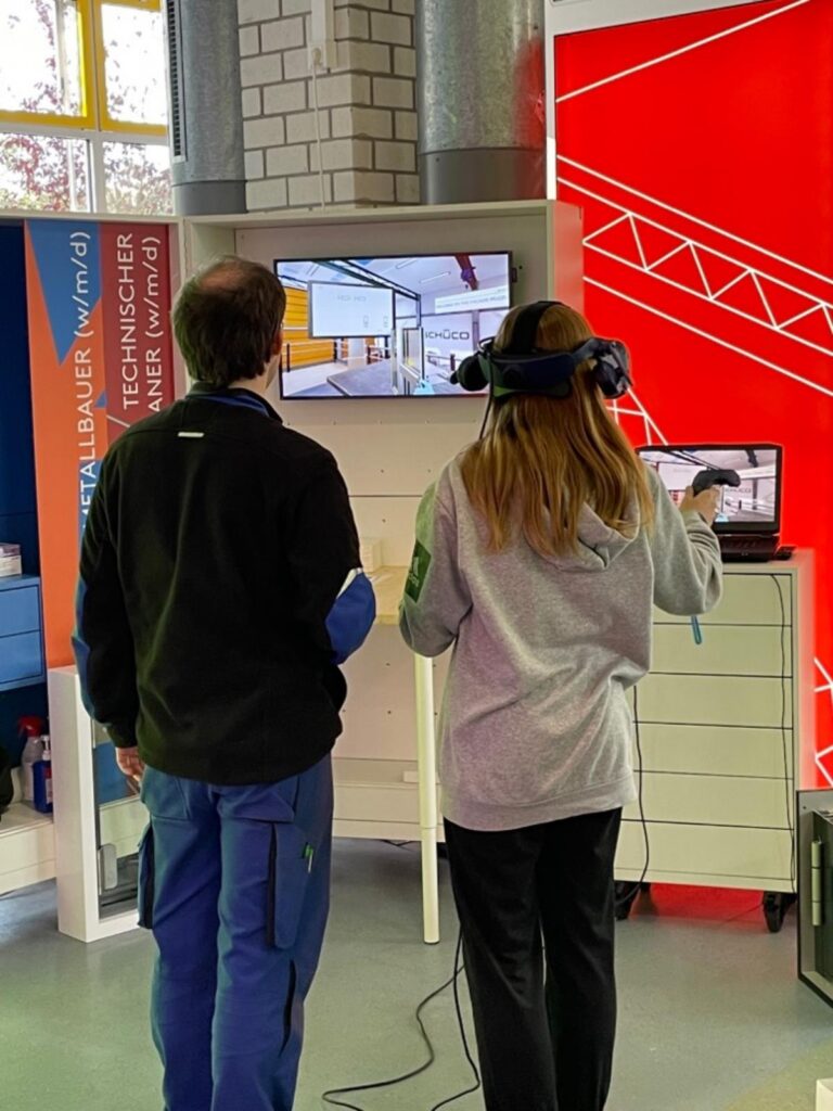 Zwei Personen mit VR-Headsets interagieren mit einem Bildschirm.