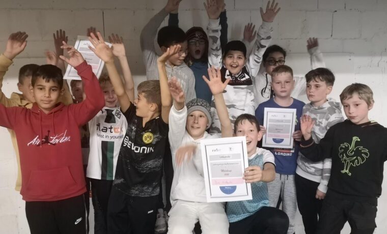Gruppe von Kindern in einem Raum, die fröhlich mit Zertifikaten posieren.