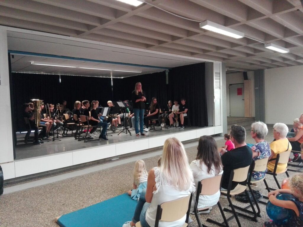 Schüler spielen in einem Raum ein Konzert, Publikum sitzt auf Stühlen.