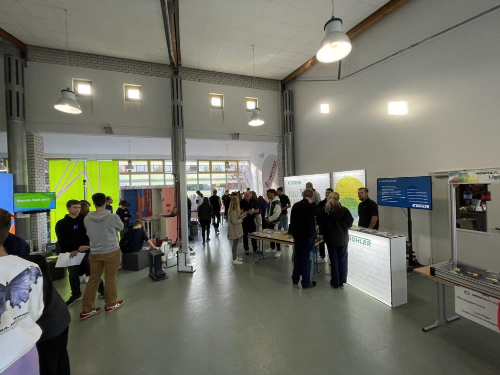 Messe mit mehreren Ständen und Besuchern in einem großen Raum.
