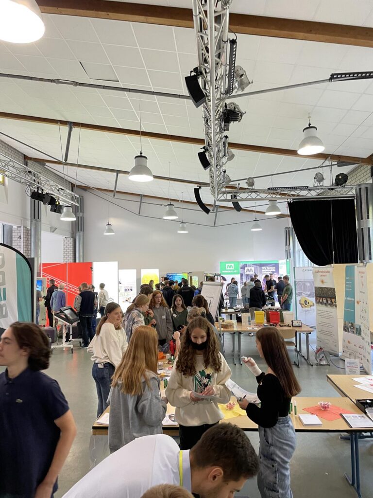 Schüler und Schülerinnen arbeiten an Tischen in einer Schulveranstaltung.