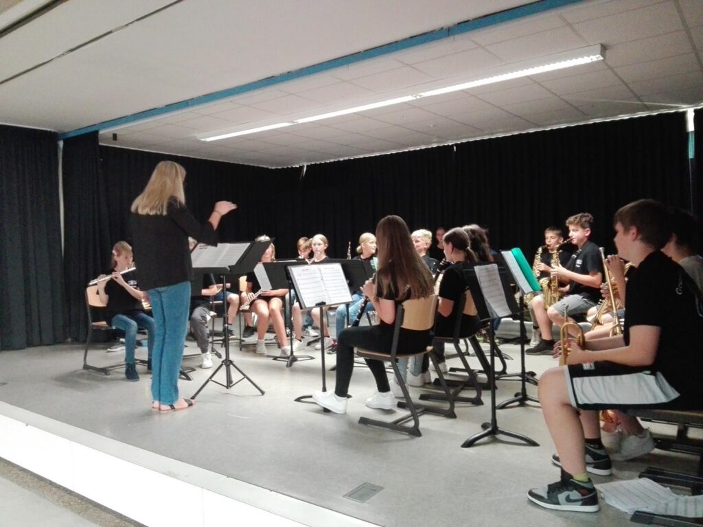Proben einer Schulband auf einer Bühne mit einer Dirigentin.