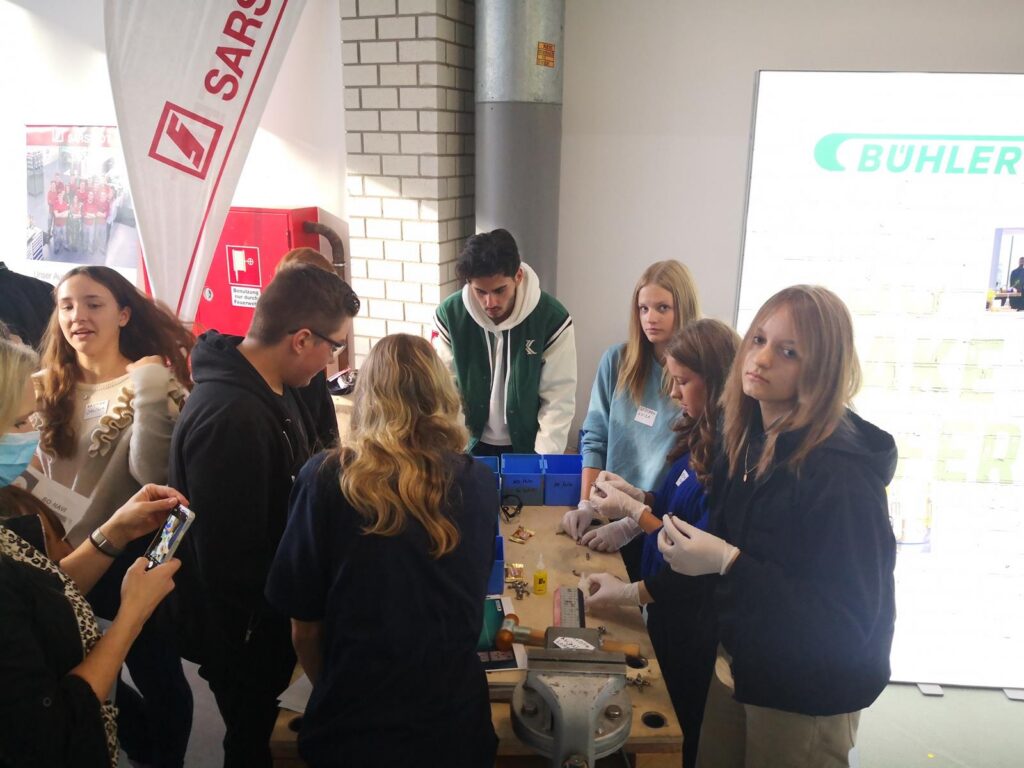 Schüler arbeiten an einem Projekttisch, umgeben von Materialien und Geräten.