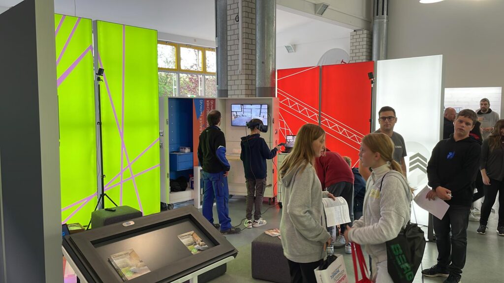 Messehalle mit bunten Ständen und Besuchern, die sich informieren.