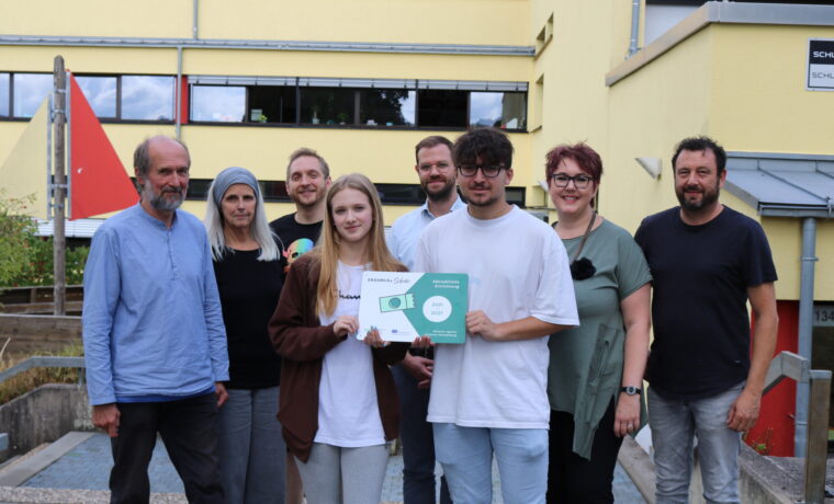 Gruppe von Personen, die ein Zertifikat vor einem Schulgebäude präsentieren.
