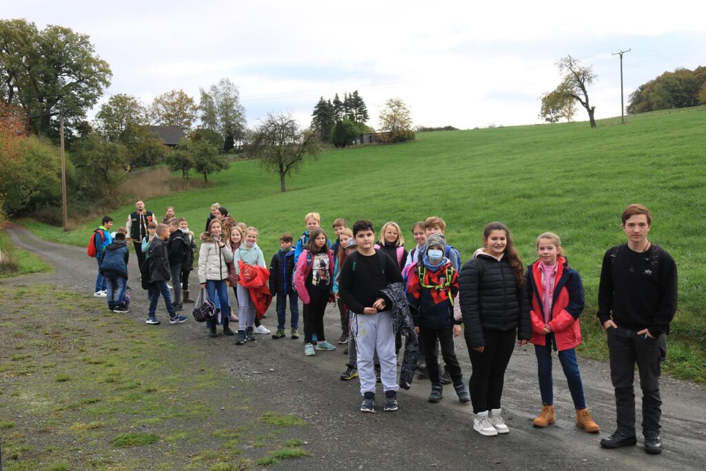 Gruppe von Schülern auf einem Feldweg, umgeben von Wiesen und Bäumen.