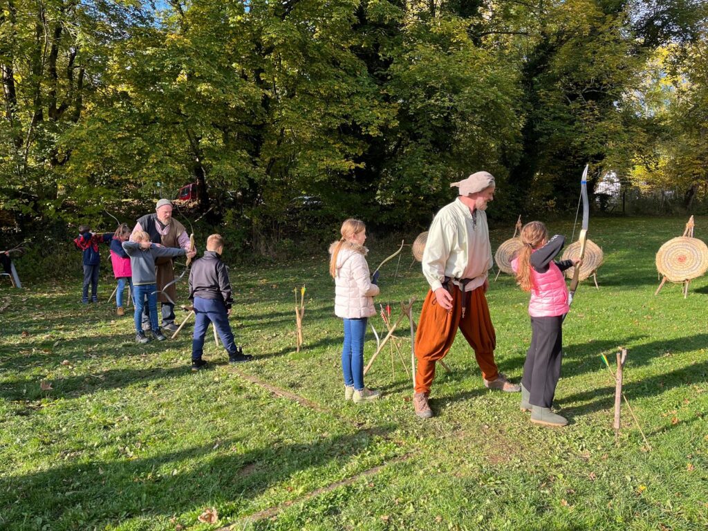 Kinder üben das Bogenschießen unter Anleitung in einem grünen Park.
