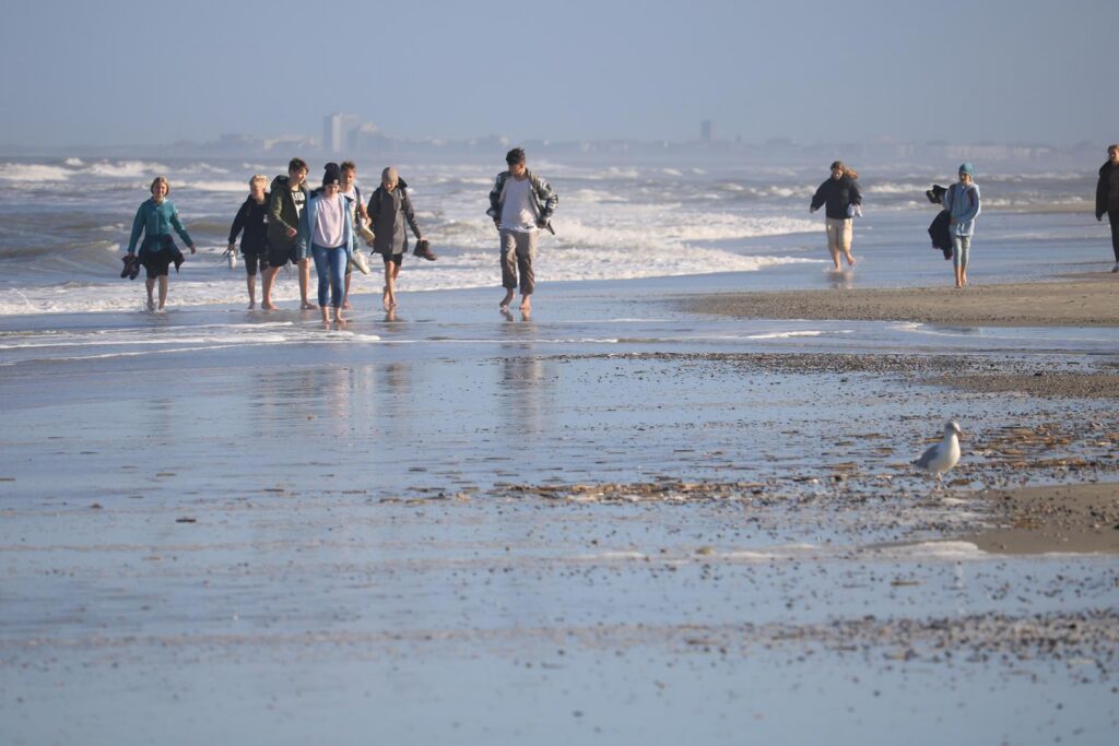 Menschen spazieren am Strand entlang, Wellen schlagen sanft ans Ufer.