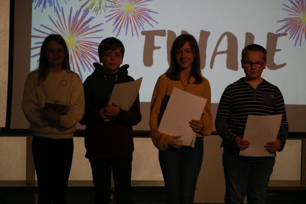 Vier Schüler stehen auf einer Bühne und halten Papiere in der Hand.
