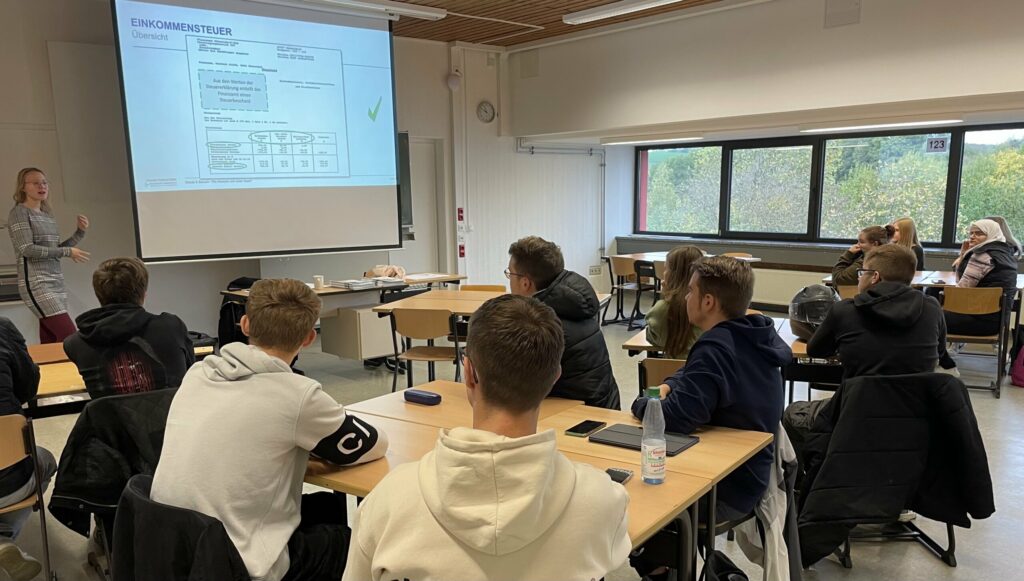 Lehrerin präsentiert an der Tafel vor einer Klasse von Schülerinnen und Schülern.