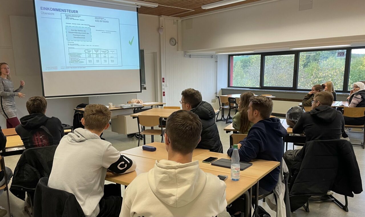 Lehrerin präsentiert an der Tafel vor einer Klasse von Schülerinnen und Schülern.