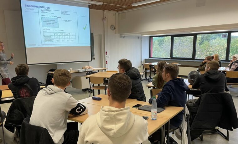 Lehrerin präsentiert an der Tafel vor einer Klasse von Schülerinnen und Schülern.