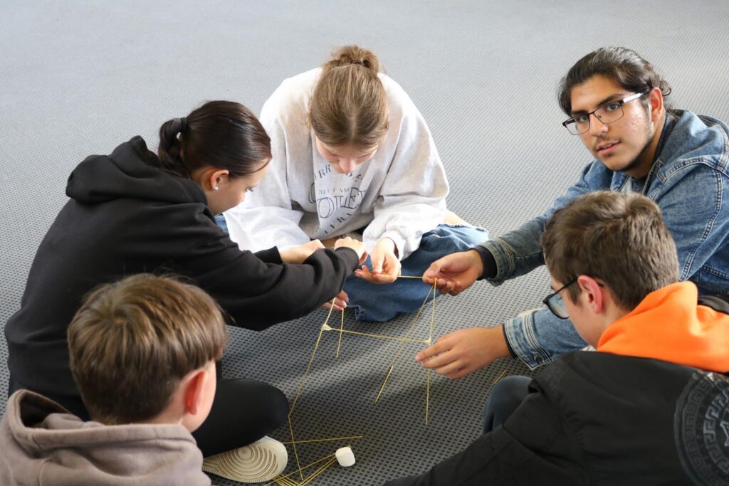Schüler arbeiten gemeinsam an einem Gruppenprojekt mit Spaghetti und Marshmallows.