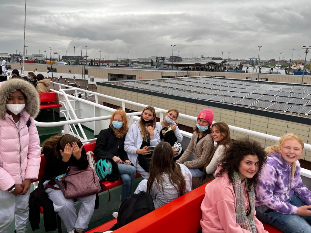 Gruppe von Kindern und Teenagern auf einem Schiff mit Masken, grauem Himmel im Hintergrund.