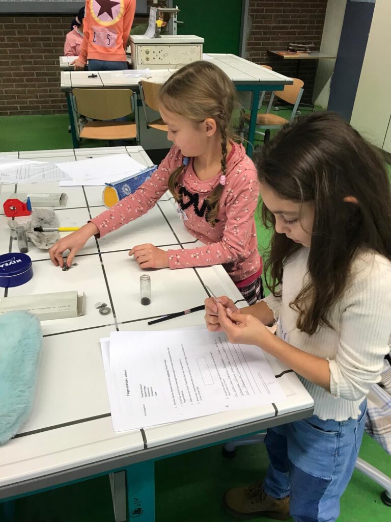 Zwei Mädchen arbeiten an einem Tisch mit Experimentiermaterialien.