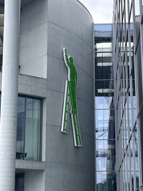 Grüne Figur auf einer Leiter an einer Gebäudewand befestigt.